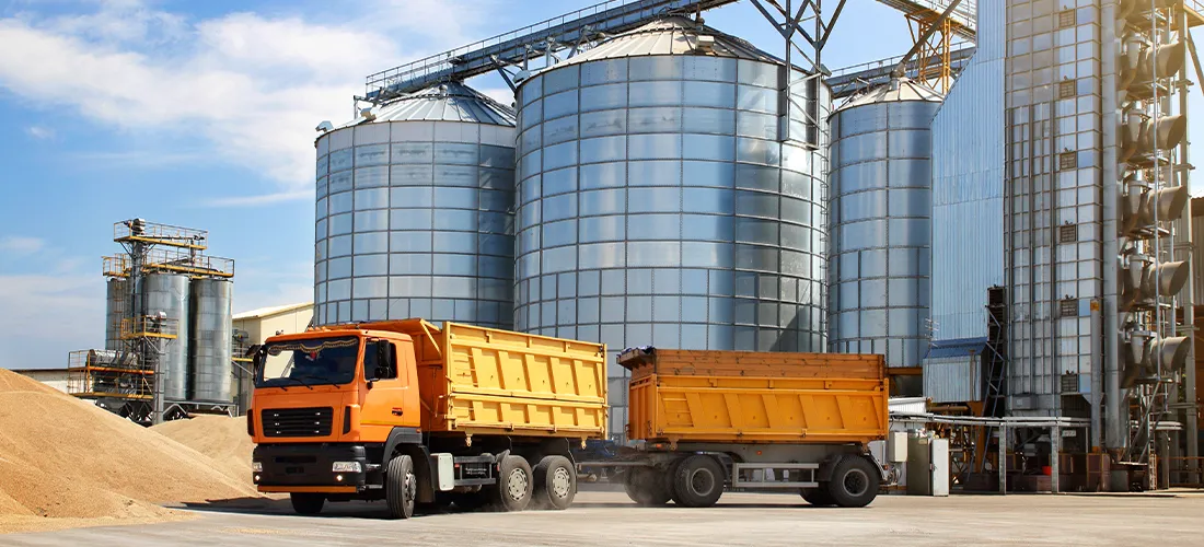 Caminhão de silo agrícola de cor laranja no território de armazenamento de grãos em clima ensolarado.